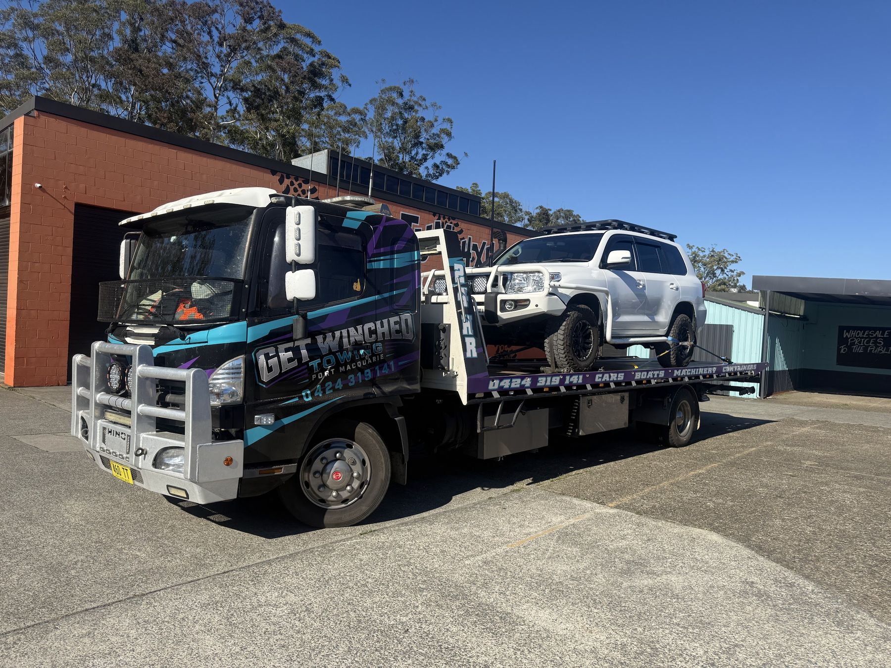 Get Winched Towing's black tilt tray truck, wrapped in teal and violet, carrying a white LandCruiser