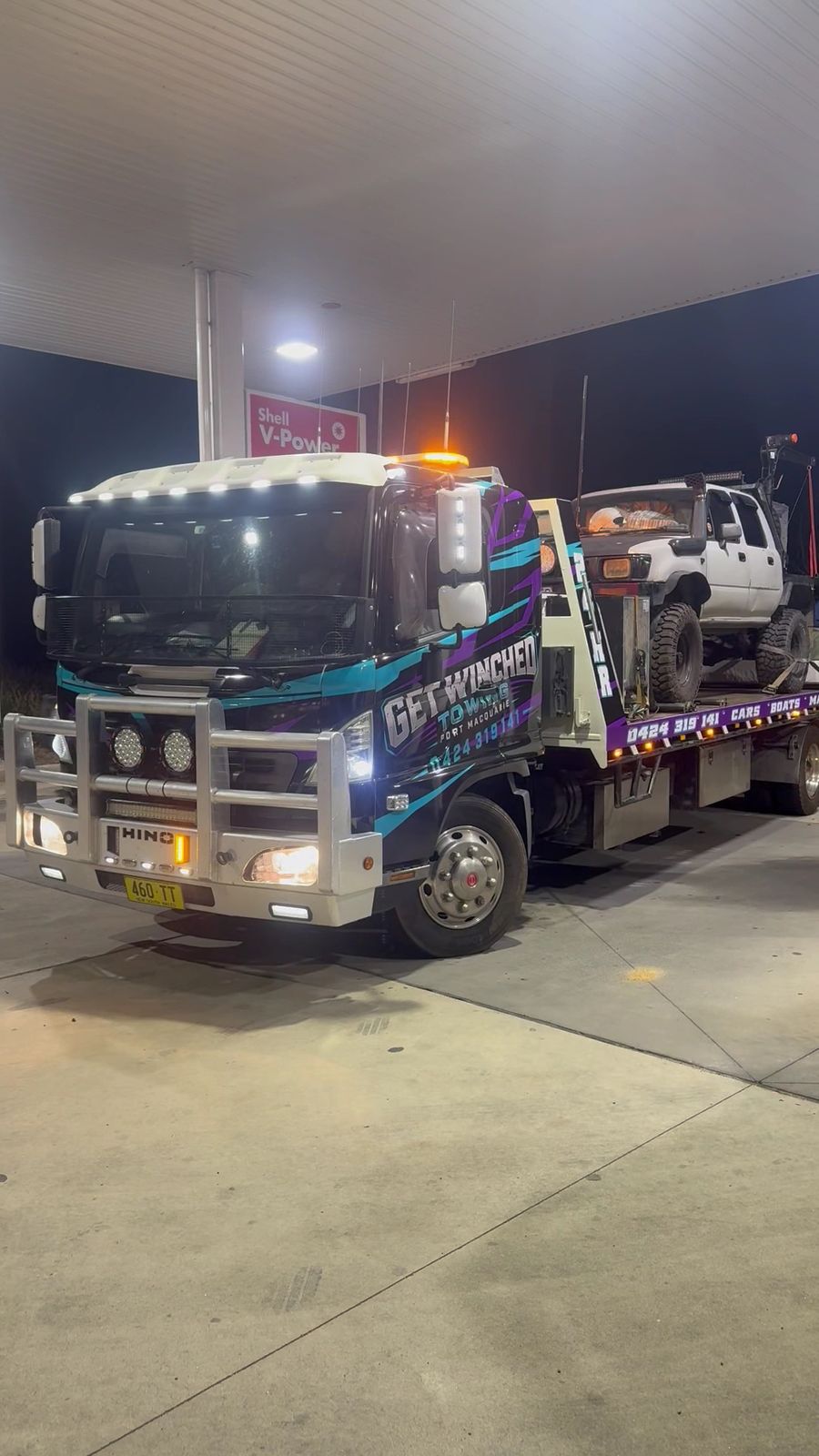 The Get Winched truck under servo lights at night with a car loaded on the back