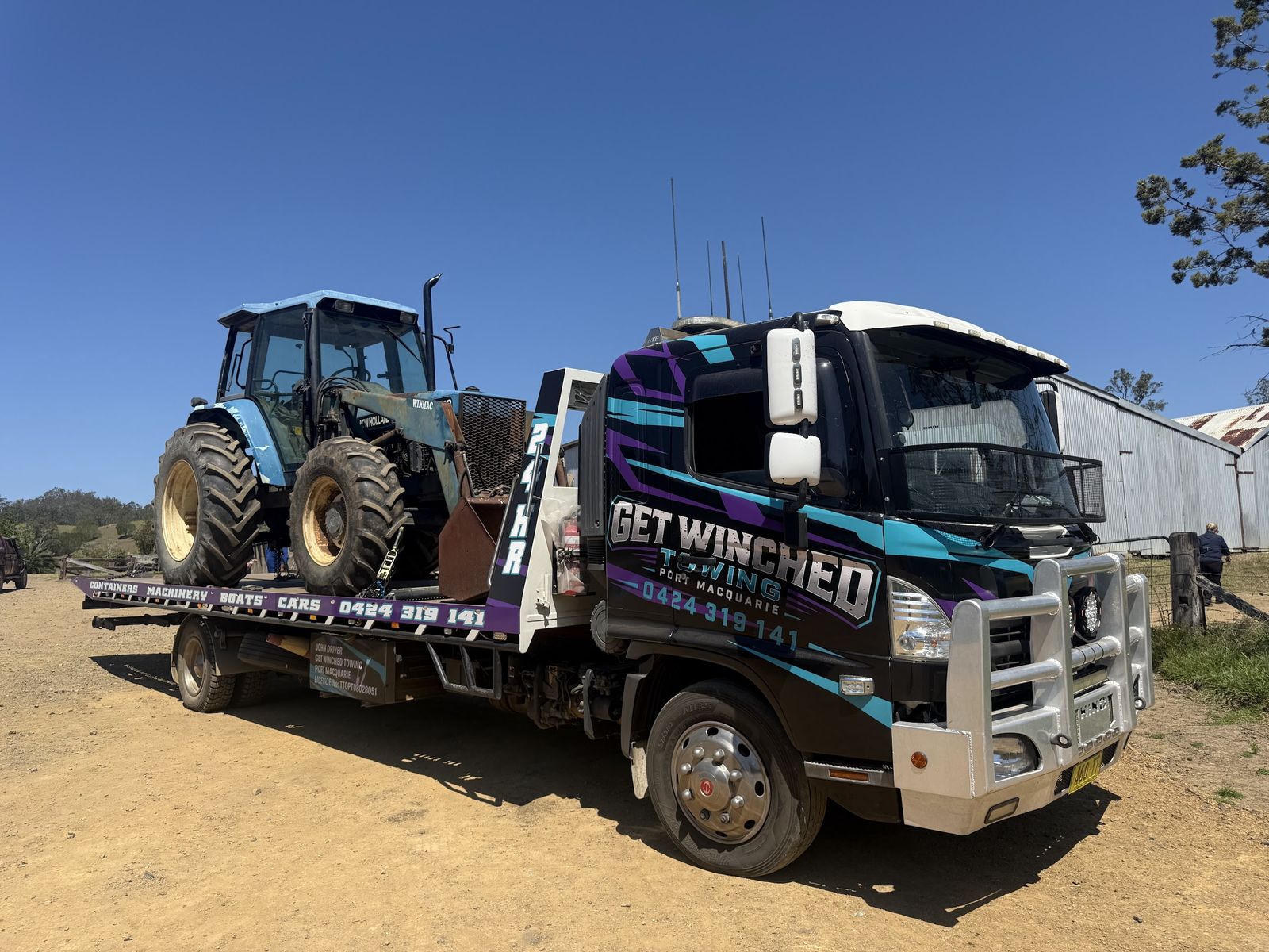 Blue Ford tractor loaded on the Get Winched tilt tray in a dry yard